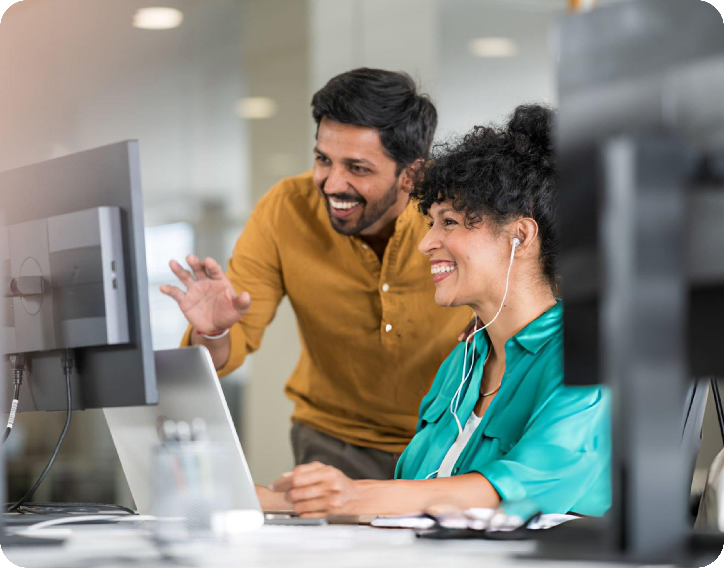 Two colleagues smiling while reviewing work together on a desktop computer